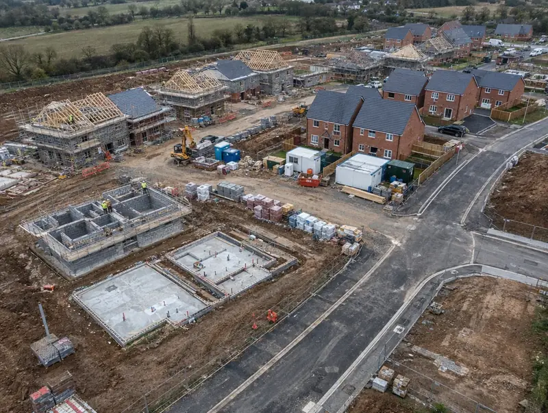 Aerial view of a housing site with plots at different build stages and a site compound