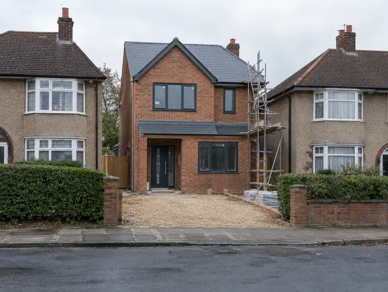 New brick house nearing completion on an infill plot between two 1930s semi-detached houses
